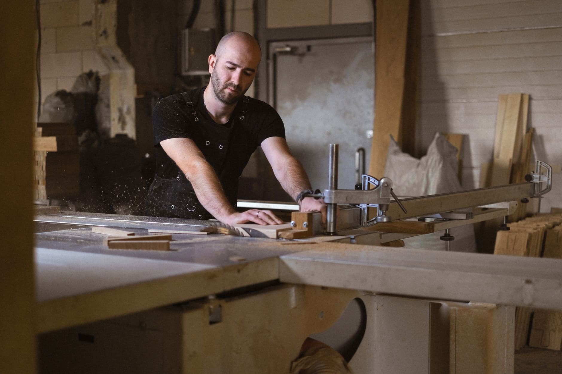 A carpenter using a bench saw in a workshop with timber dust collection fitted