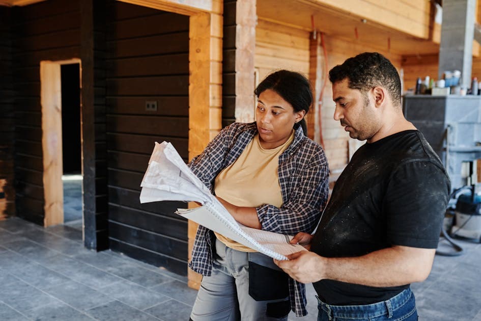 builder in workwear talking with a homeowner at a house extension site, documents in hand