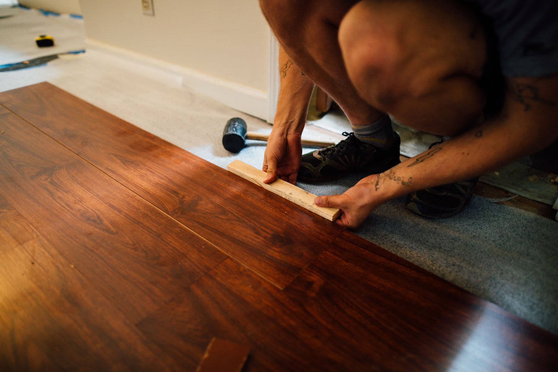 A flooring installer laying vinyl flooring wearing knee pads and gloves
