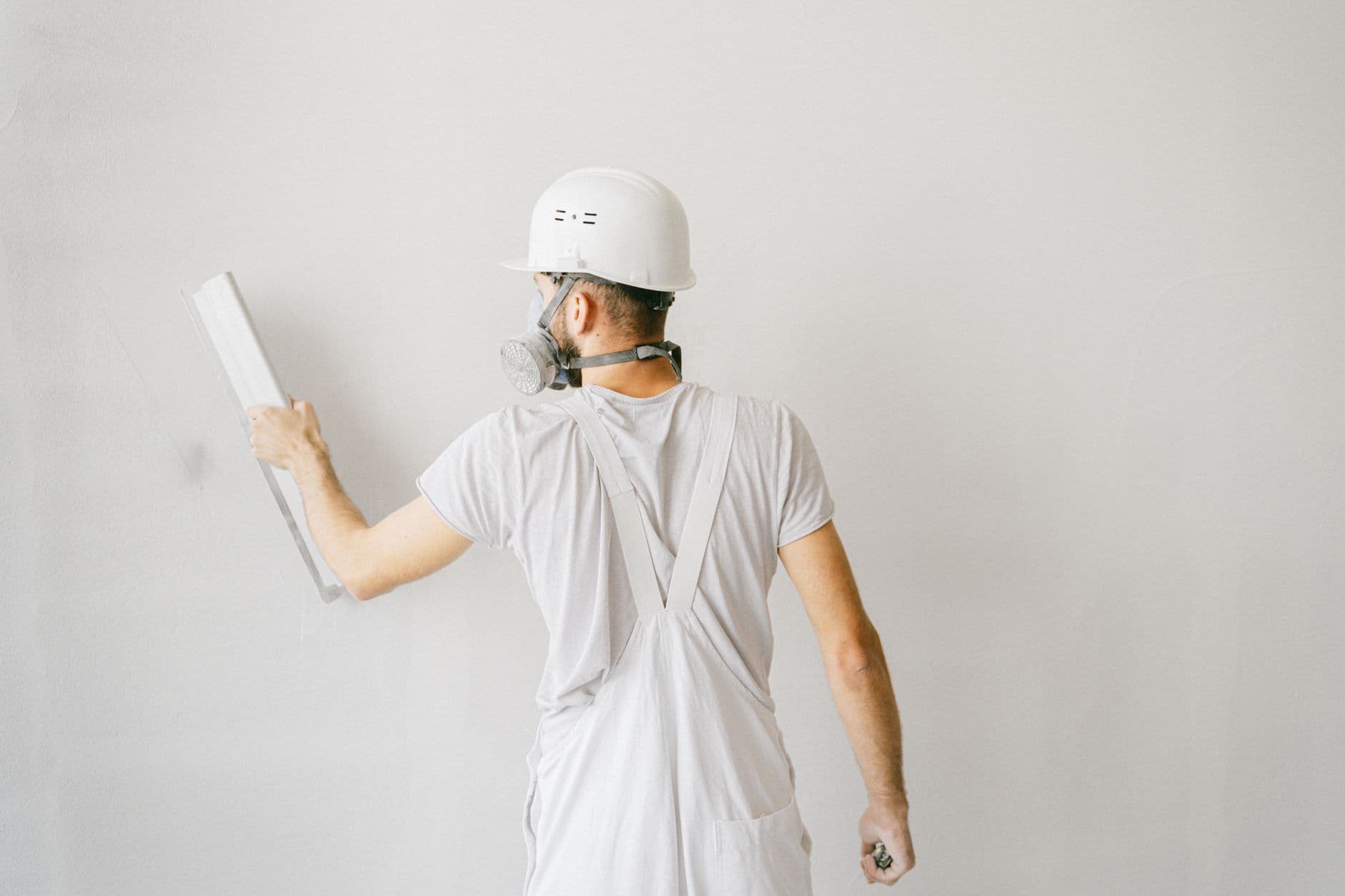 A plasterer applying render to an interior wall wearing a dust mask and safety goggles