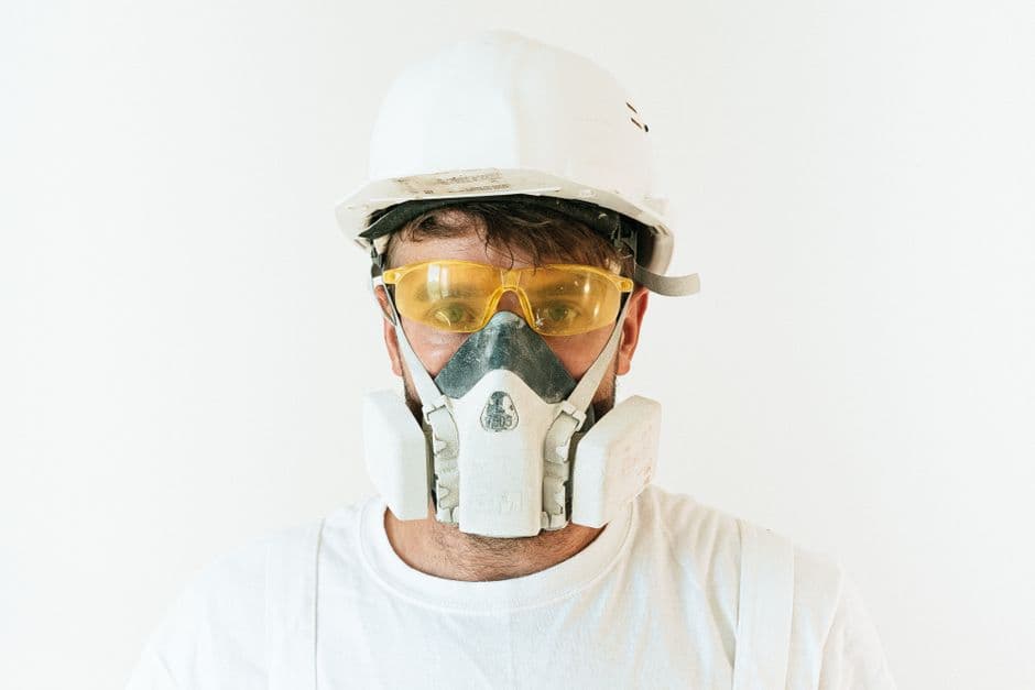 A builder wearing a respirator and gloves while working with cement