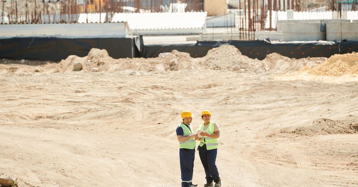 A site manager talking one to one with a construction worker in a hi-vis vest and hard hat in a quiet corner of a site